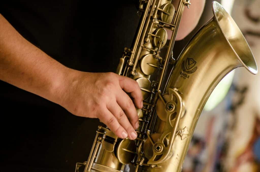 A detailed view of a musician's hand playing a gold saxophone outdoors.