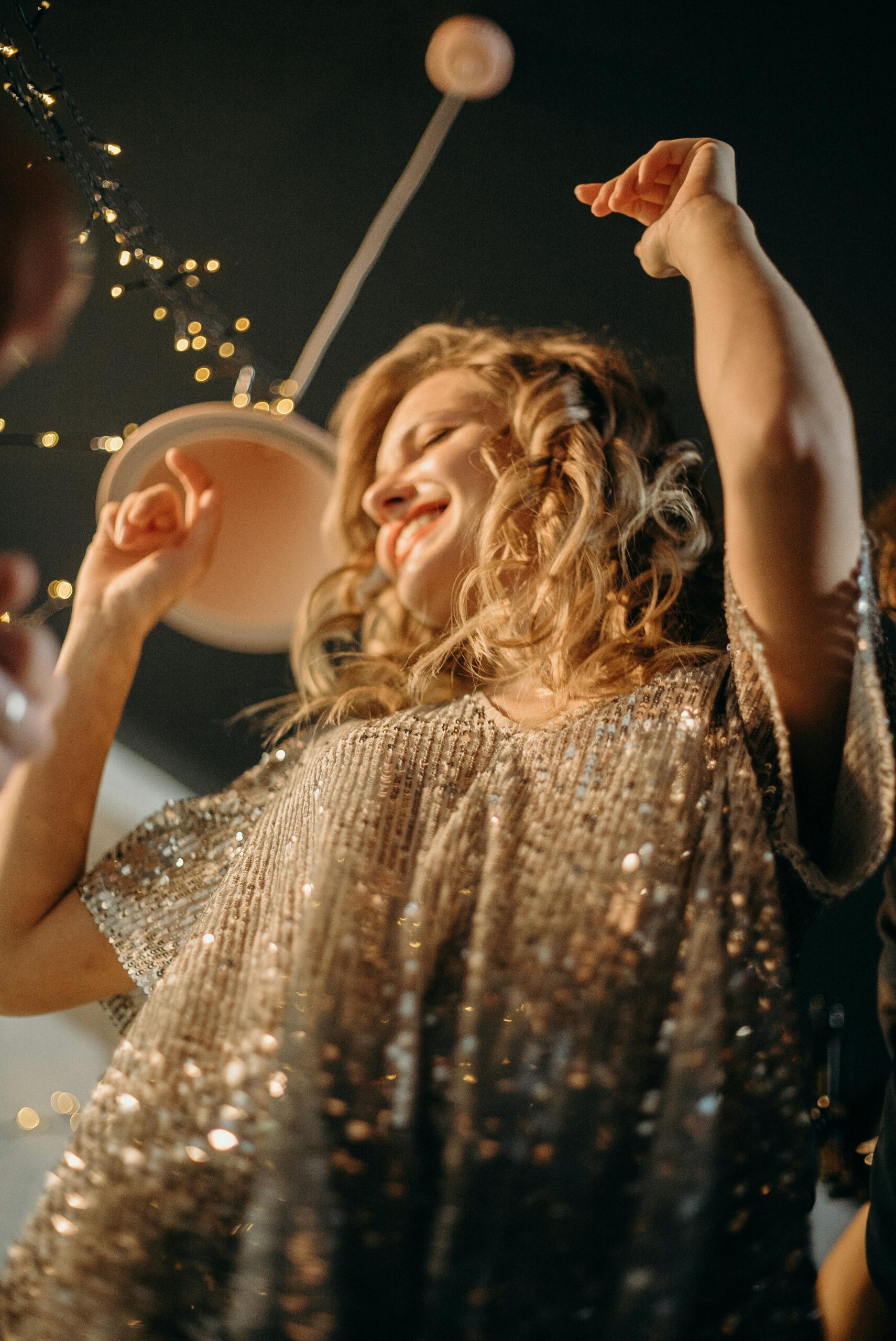 A woman joyfully dancing in a sparkling dress during a festive night party.