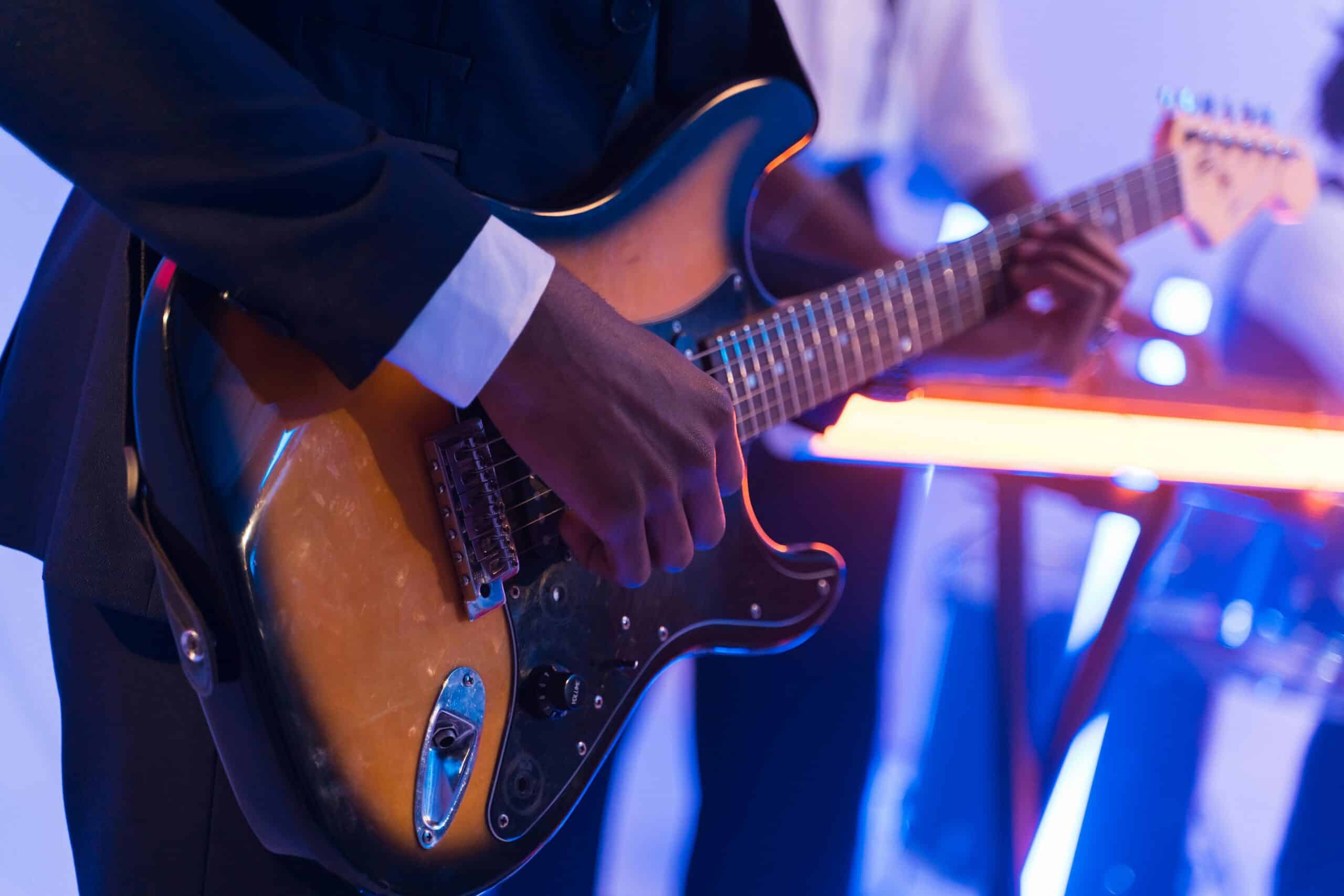 Musician playing an electric guitar on stage, focusing on hands and instrument.
