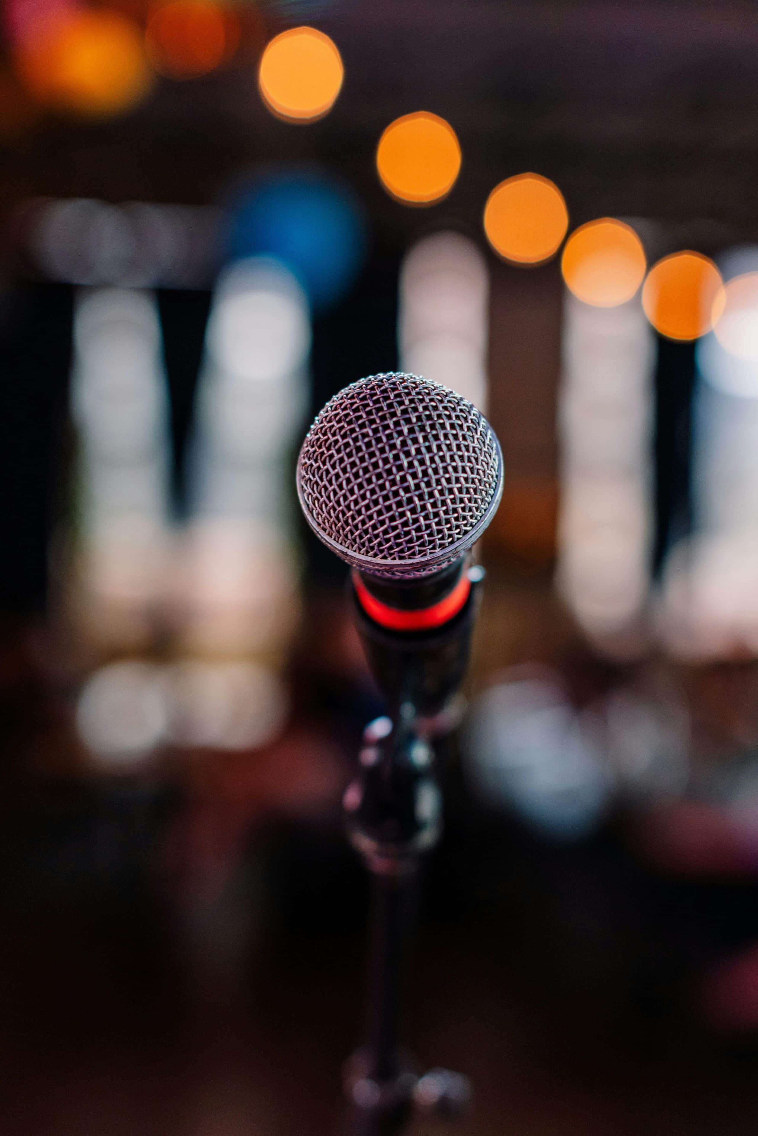 A microphone in focus with blurred bokeh lights in the background, creating a vibrant nightlife atmosphere.