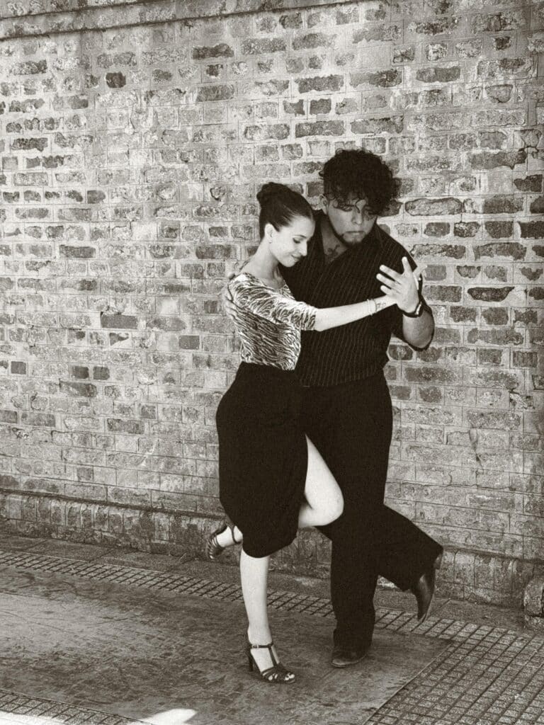 A couple performs a passionate tango dance against a brick wall in Buenos Aires, Argentina.