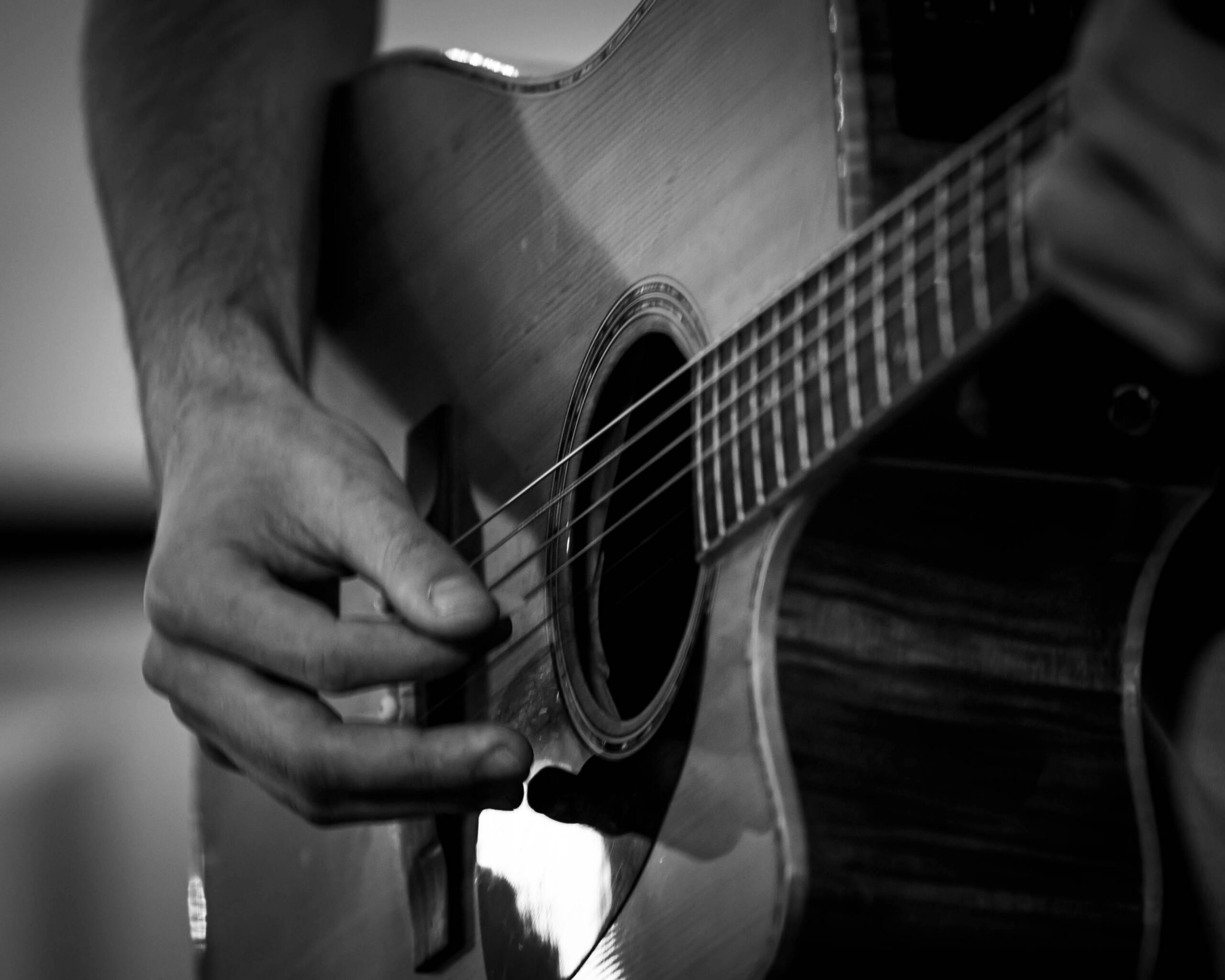 Detailed black and white shot of hands playing an acoustic guitar, focusing on strings and soundhole.